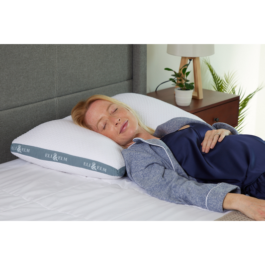 A white, rectangular side sleeper pillow with a pillowcase on a bed, against a wooden headboard background.