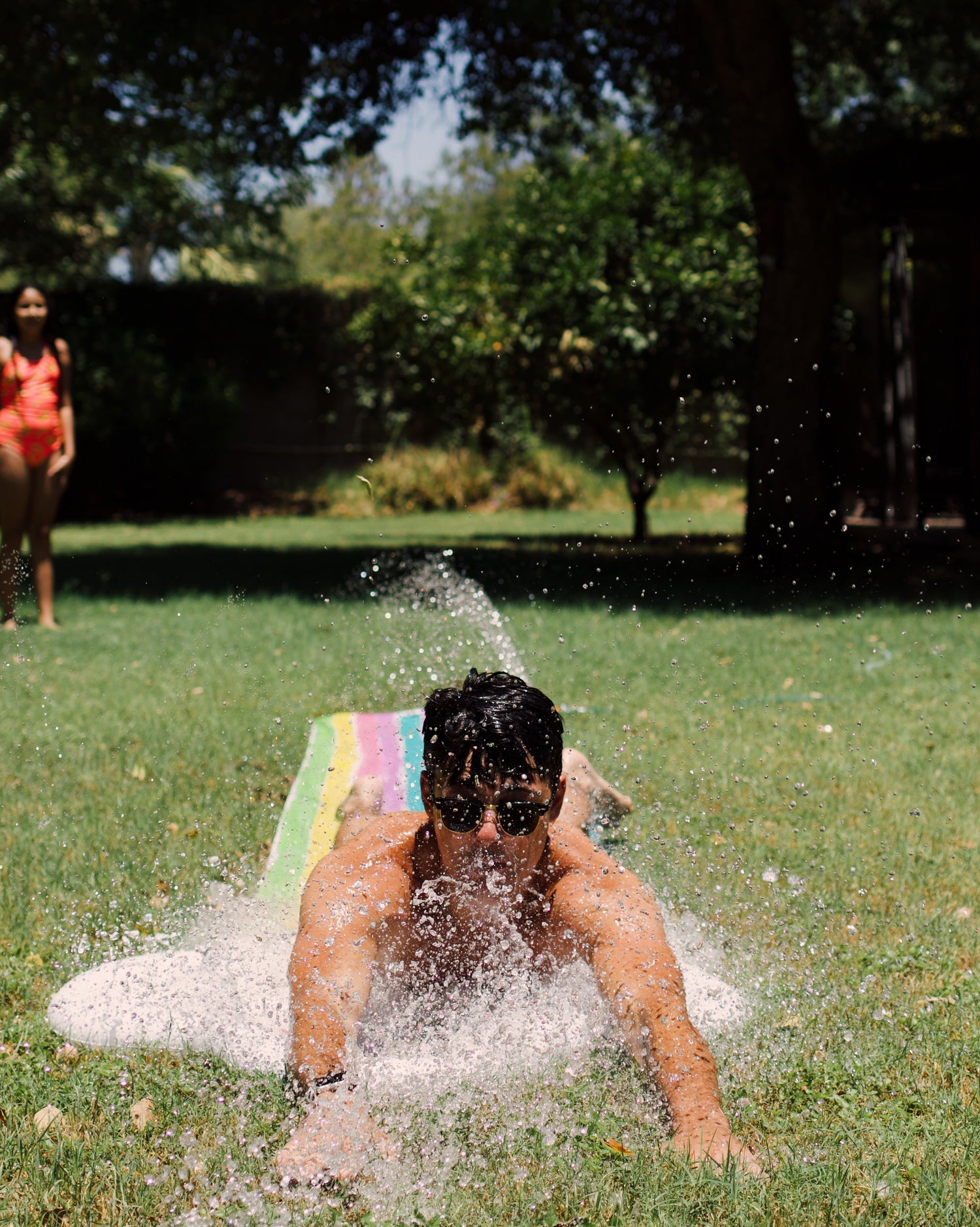 Person sliding on a slip and slide in a park with another person in the background.