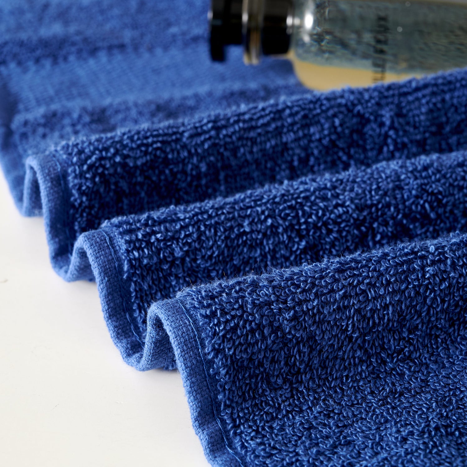 Stack of blue towels with a bottle of cleaning solution on a white background