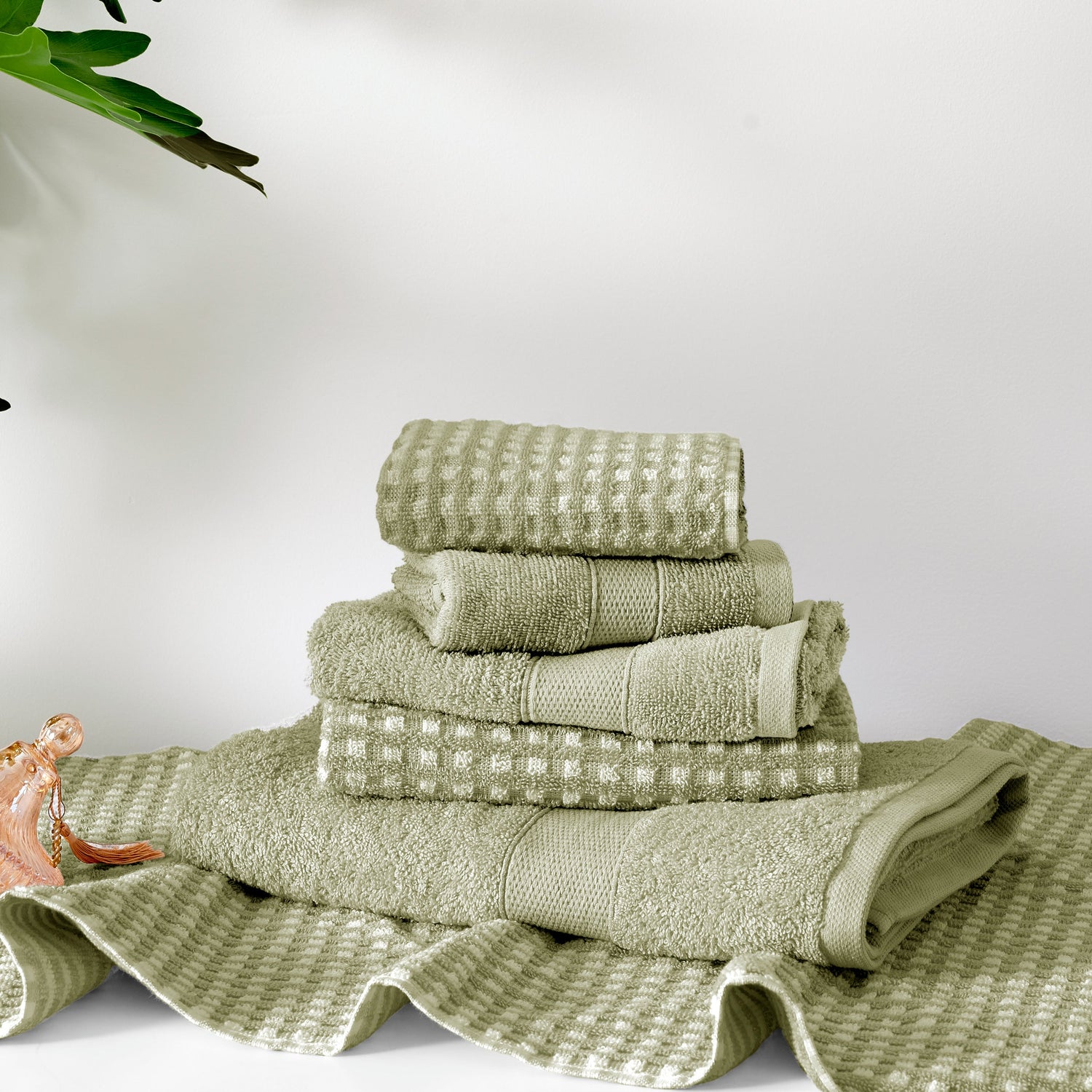 Stack of green towels on a white surface with a plant in the corner.