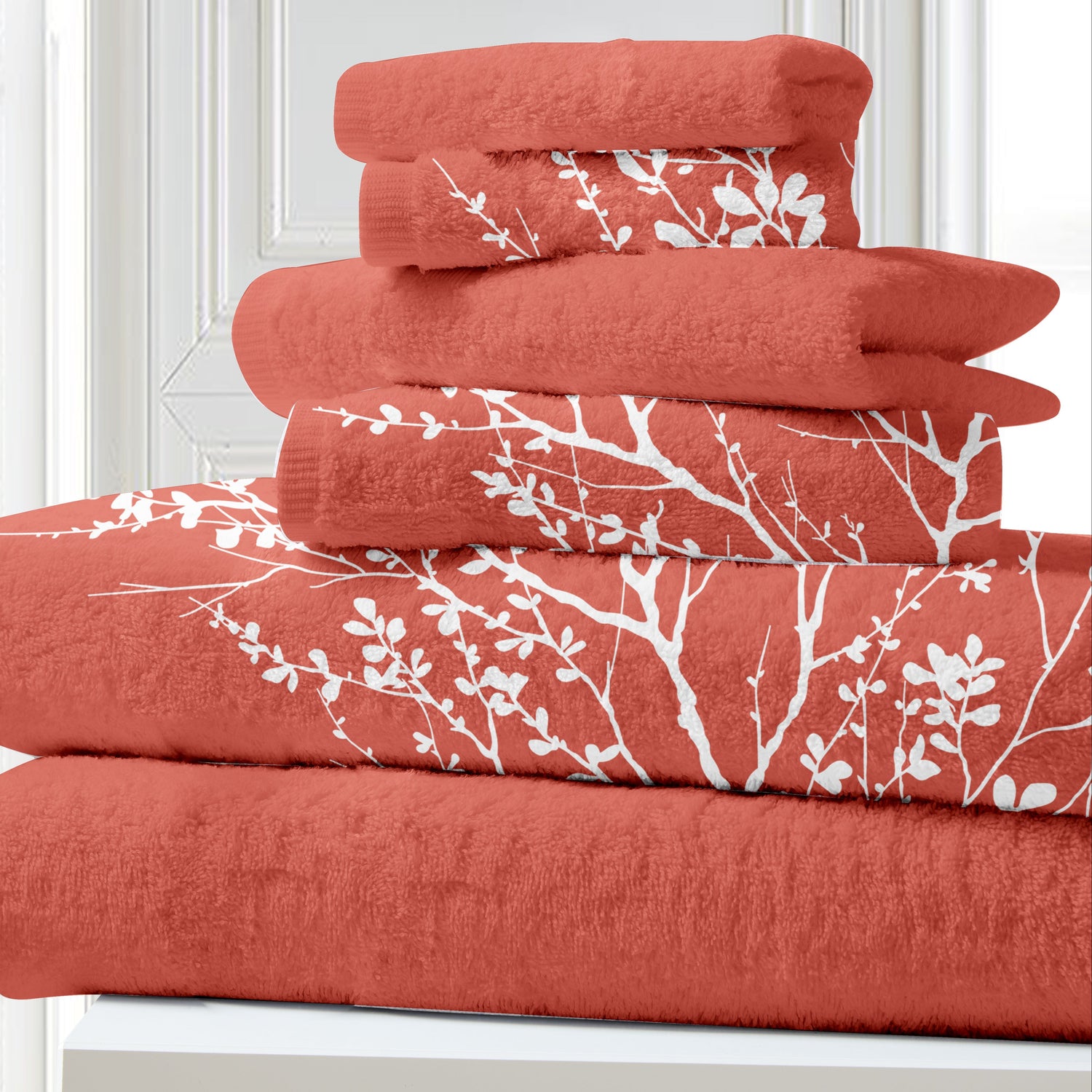Stack of red towels with white branch patterns on a white surface.