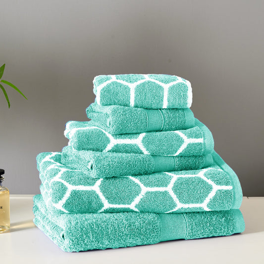 Stack of teal towels with white hexagonal patterns on a neutral background