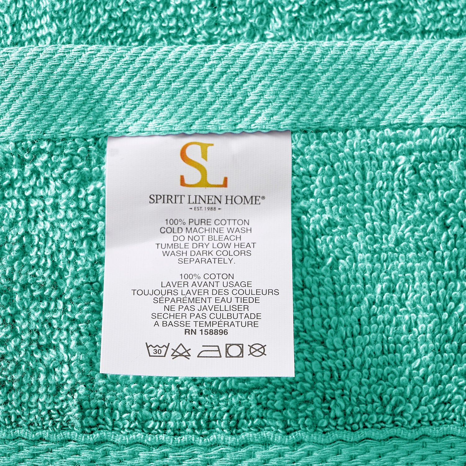 Teal towel with a label from Spirit Linen Home on a teal background