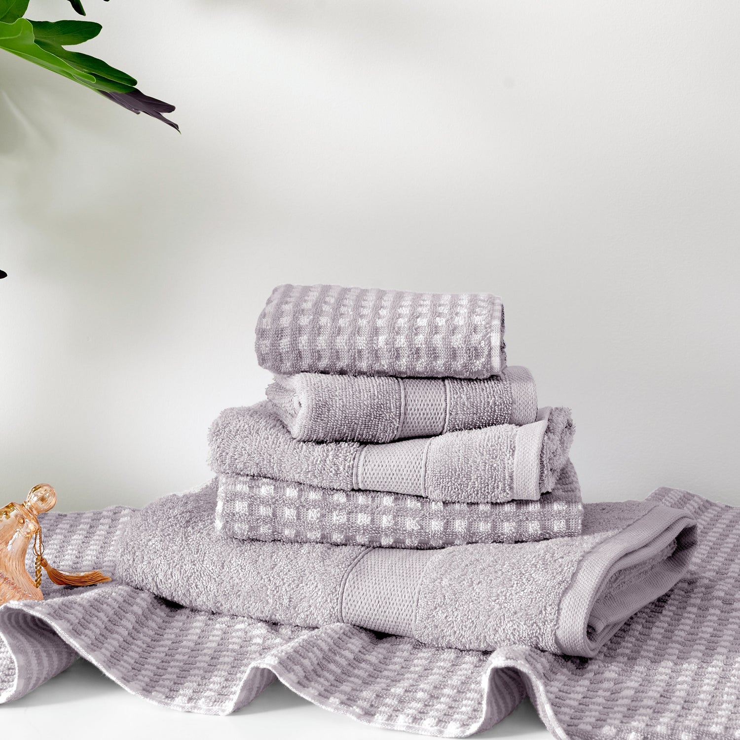 Stack of gray towels on a white surface with a plant in the corner.