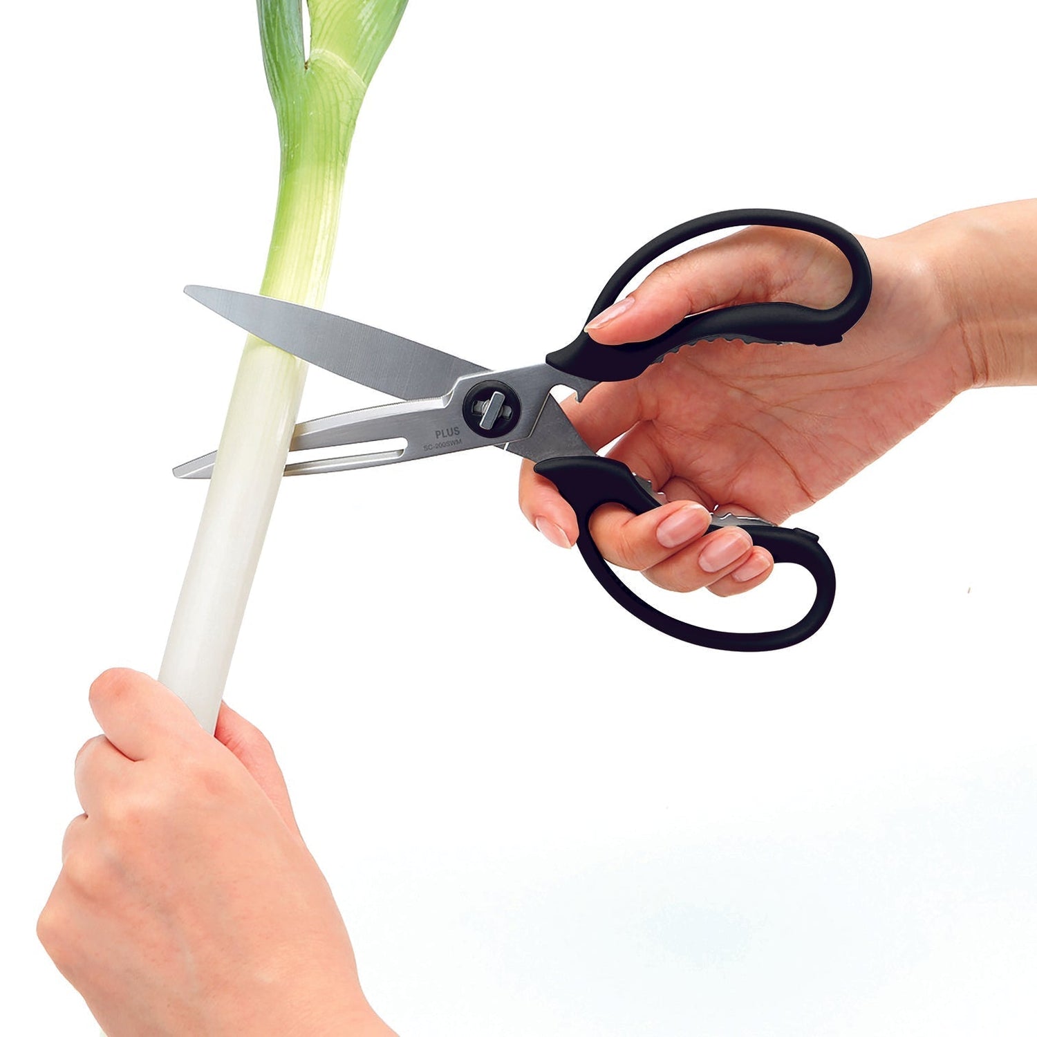 Person using kitchen shears to cut a leek on a white background