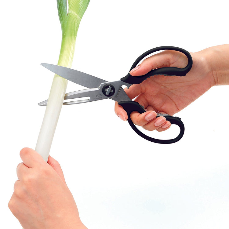 Person using kitchen shears to cut a leek on a white background