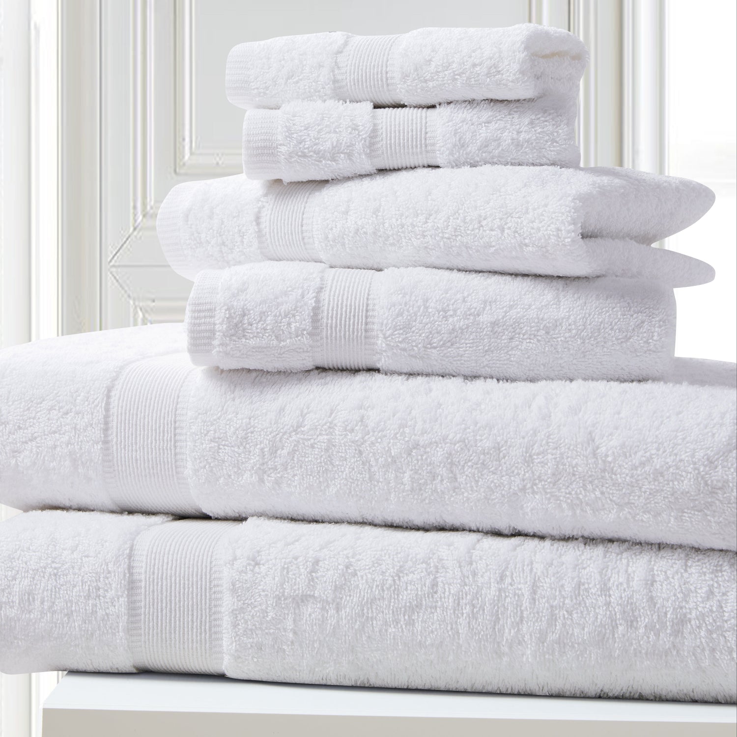 Stack of white towels on a white surface with a light gray wall background