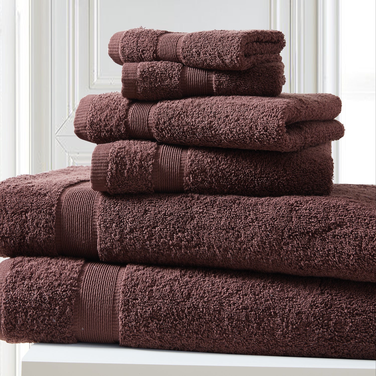 Stack of brown towels on a white surface with a light gray wall background
