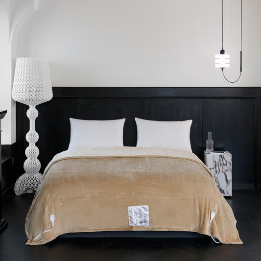 Beige electric blanket on a bed with white pillows and a lamp in the background.