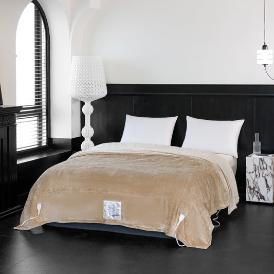 Beige electric blanket on a bed with white pillows and a lamp in the background.