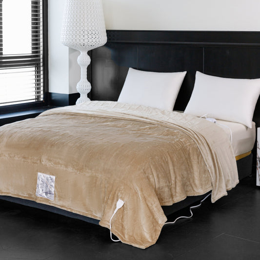 Beige electric blanket on a bed with white pillows and a lamp in the background.
