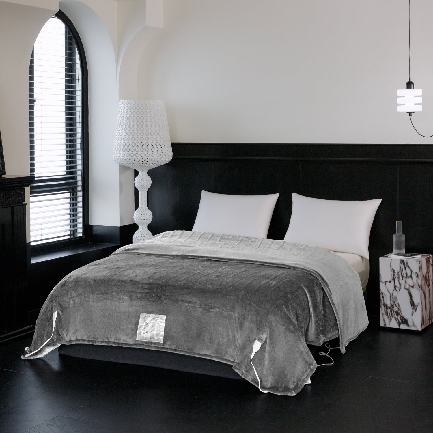 Gray blanket draped over a bed in a modern bedroom with a lamp and nightstand.
