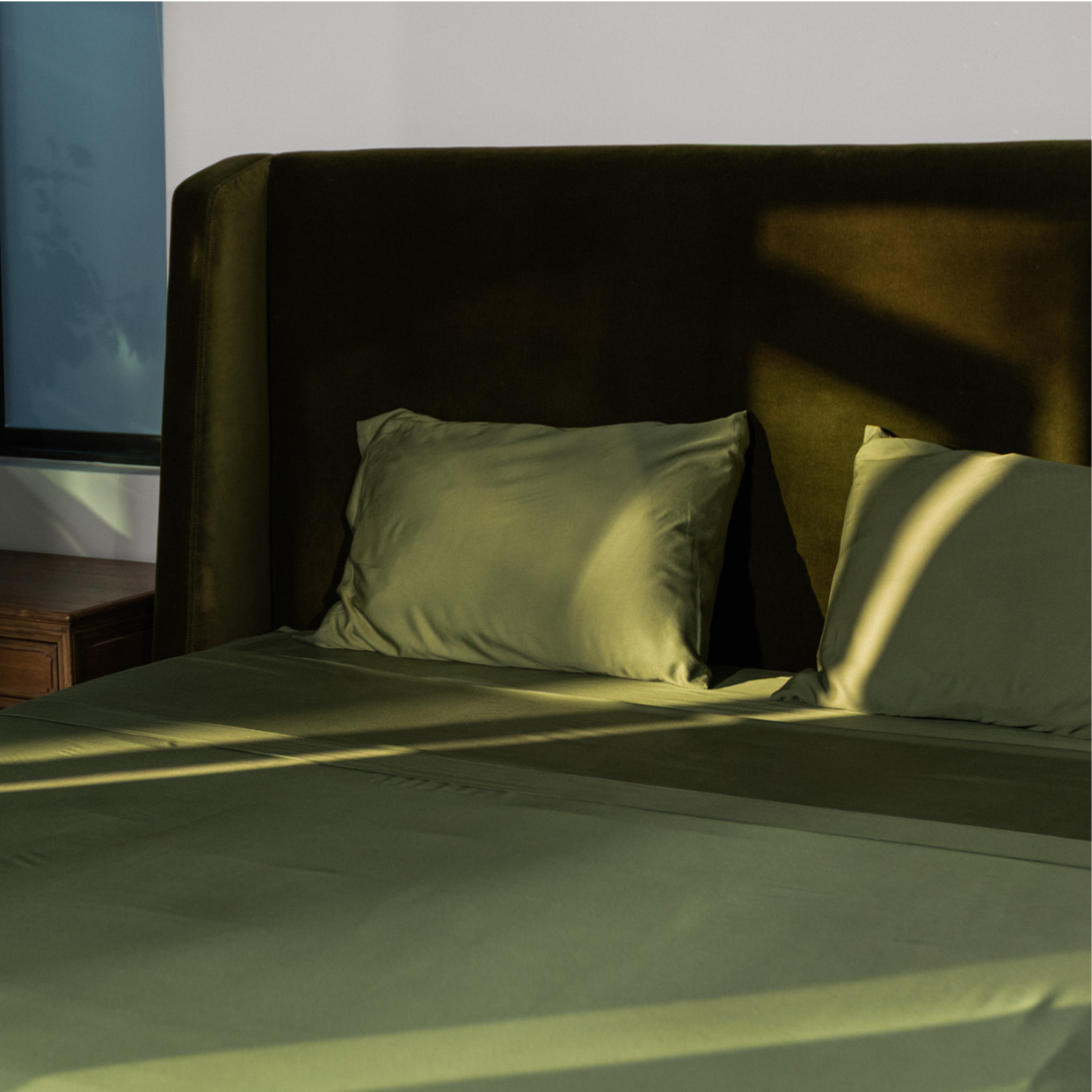 Bed with green bedding and pillows in a dimly lit room.