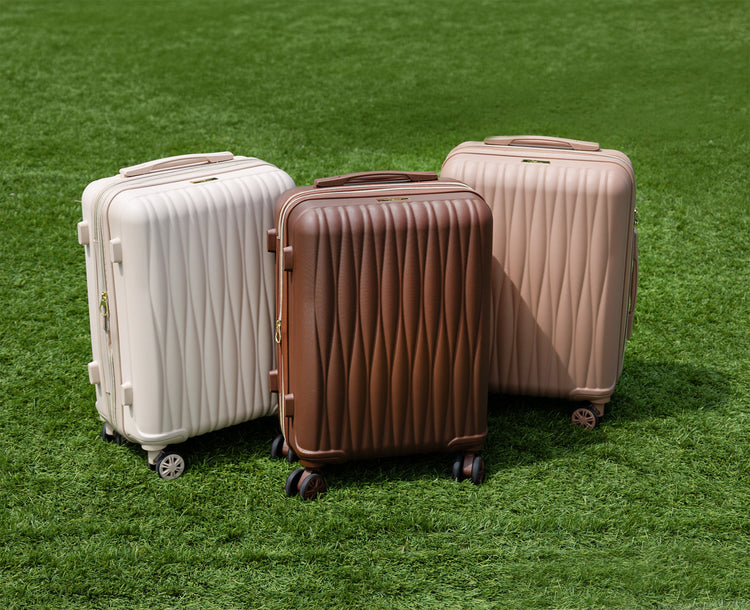 Three suitcases in white, brown, and beige on a grassy background