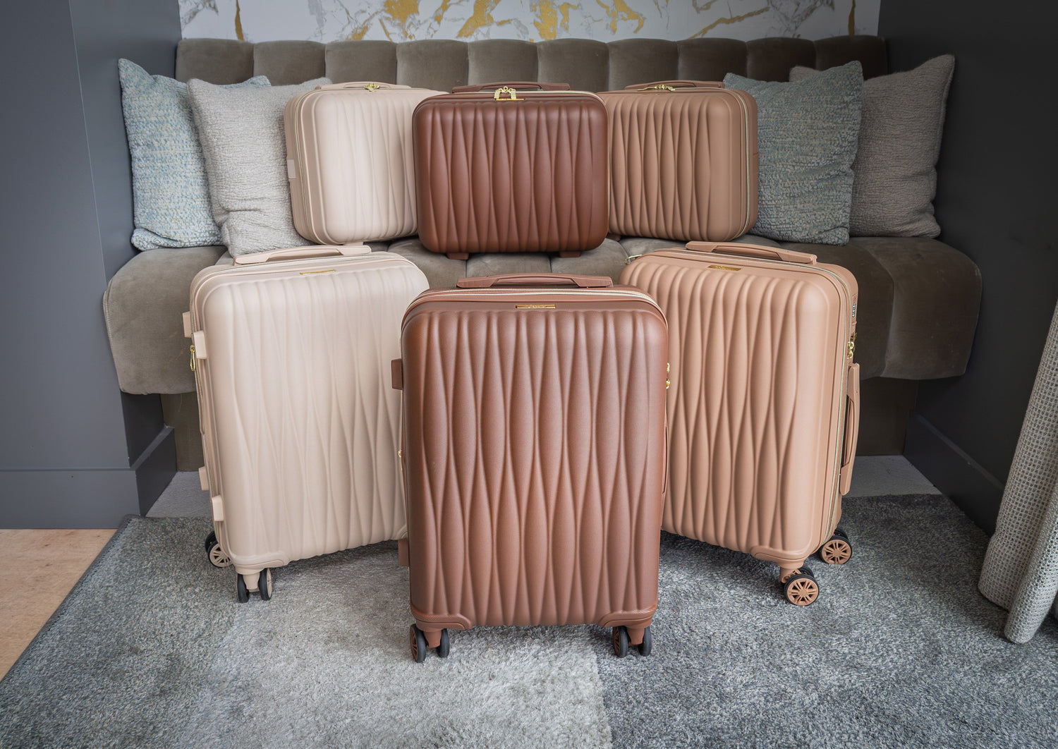 Set of brown and beige suitcases on a gray carpeted floor with a sofa in the background.