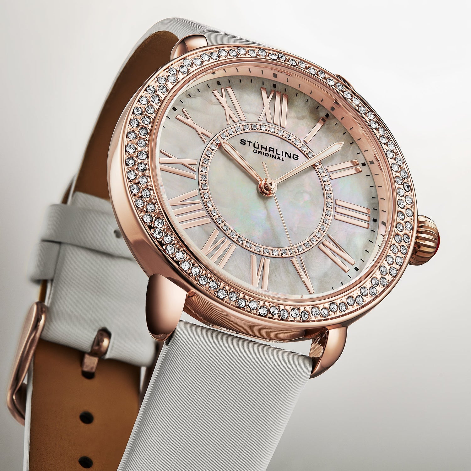 Luxury watch with rose gold case and white strap on a light background