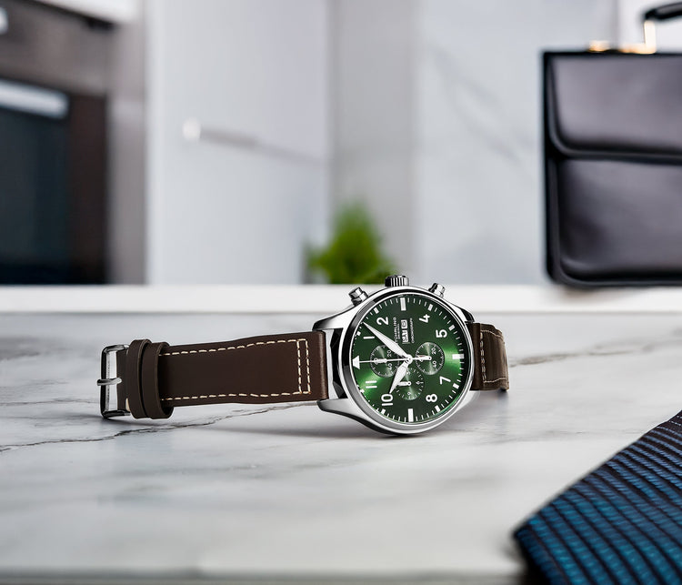 Watch with a green face and brown leather strap on a marble surface