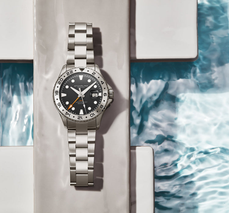 Silver watch with a black face on a textured surface with water pattern