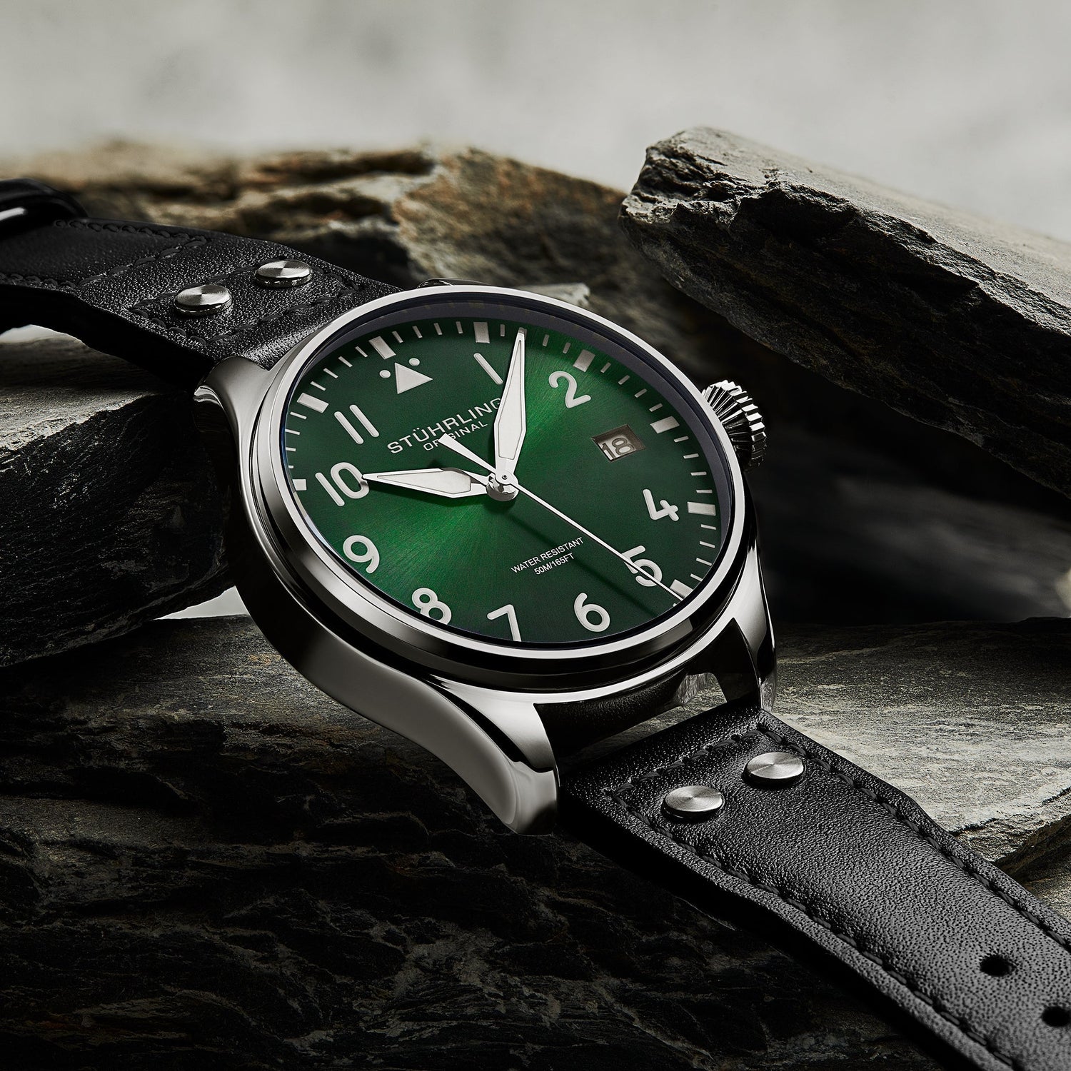 Stuhrling watch with green dial and black leather strap on a stone surface