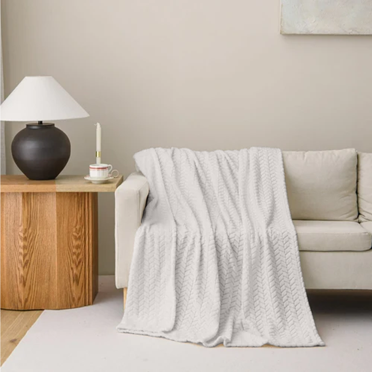 Light gray textured throw blanket draped over a beige sofa in a living room setting.