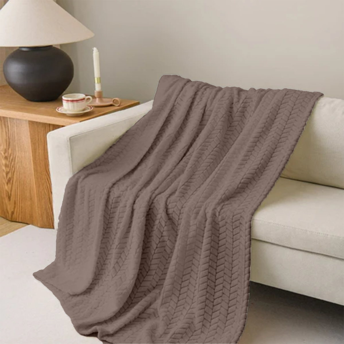 Brown knitted blanket draped over a white sofa in a cozy living room setting.