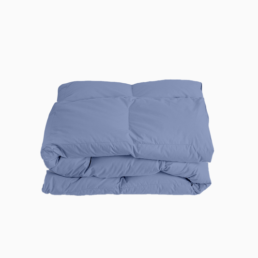 Woman peeking out from under a blue comforter in a bedroom setting