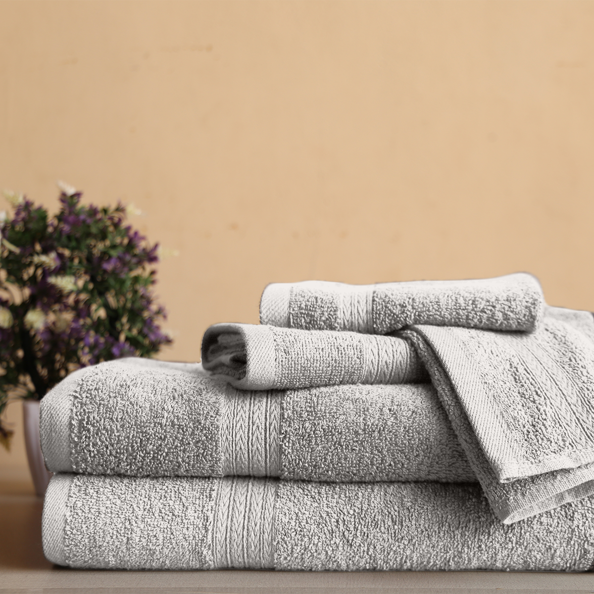 Stack of gray towels on a wooden surface with a beige wall and plant in the background