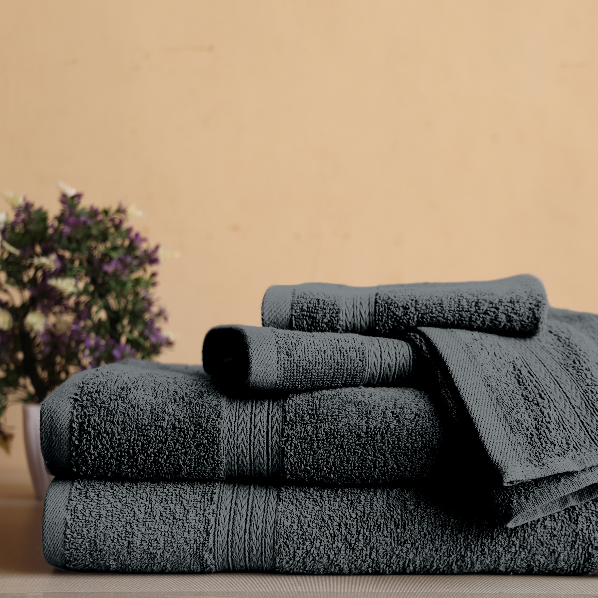 Stack of dark gray towels on a wooden surface with a blurred plant in the background