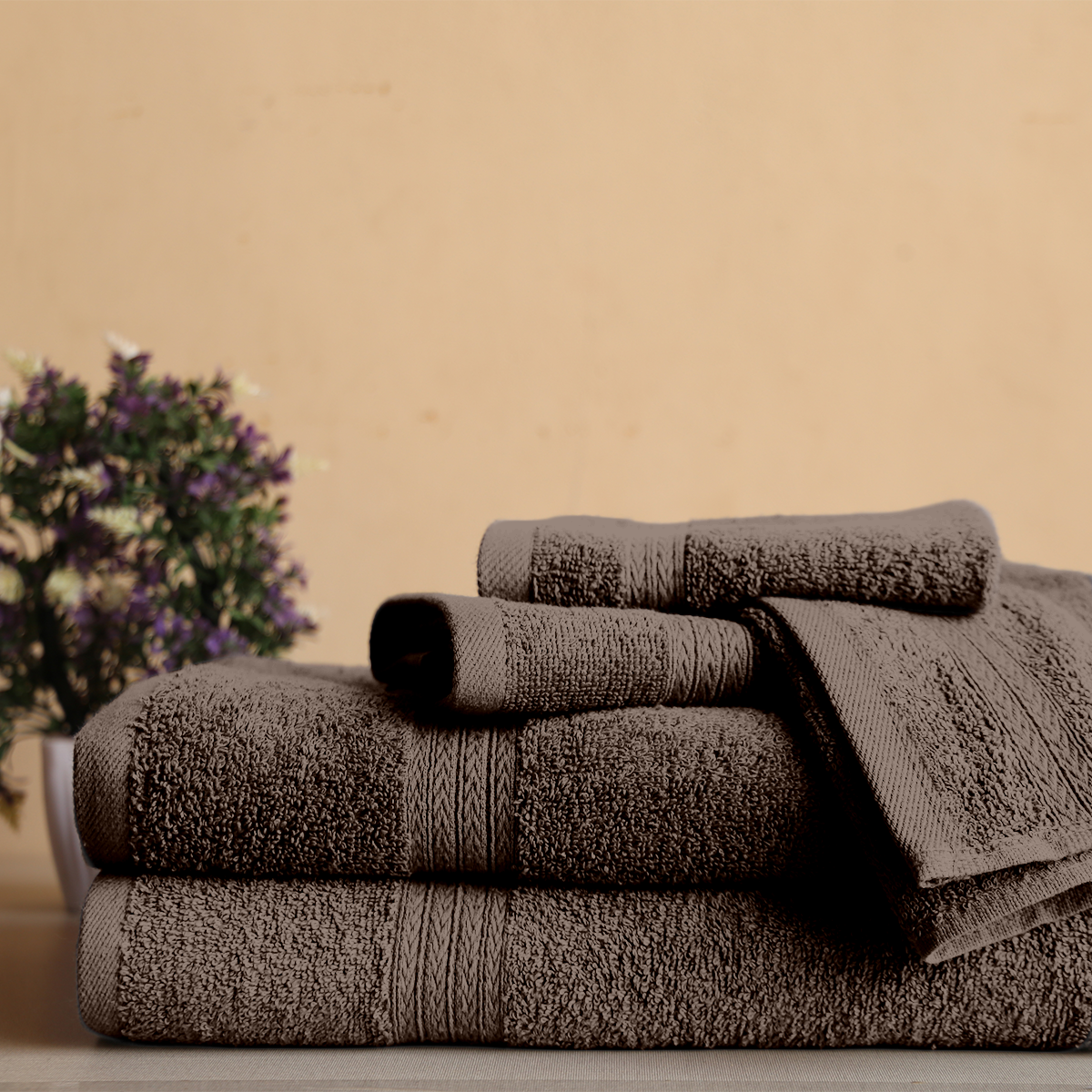 Stack of brown towels on a wooden surface with a blurred plant in the background