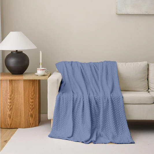 Blue blanket draped over a beige sofa in a living room setting with a wooden side table and lamp.