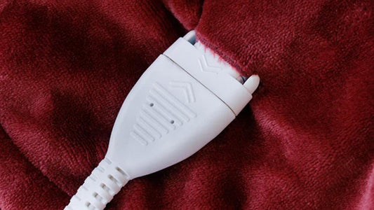 Red electric blanket draped over a white couch with power cord visible.