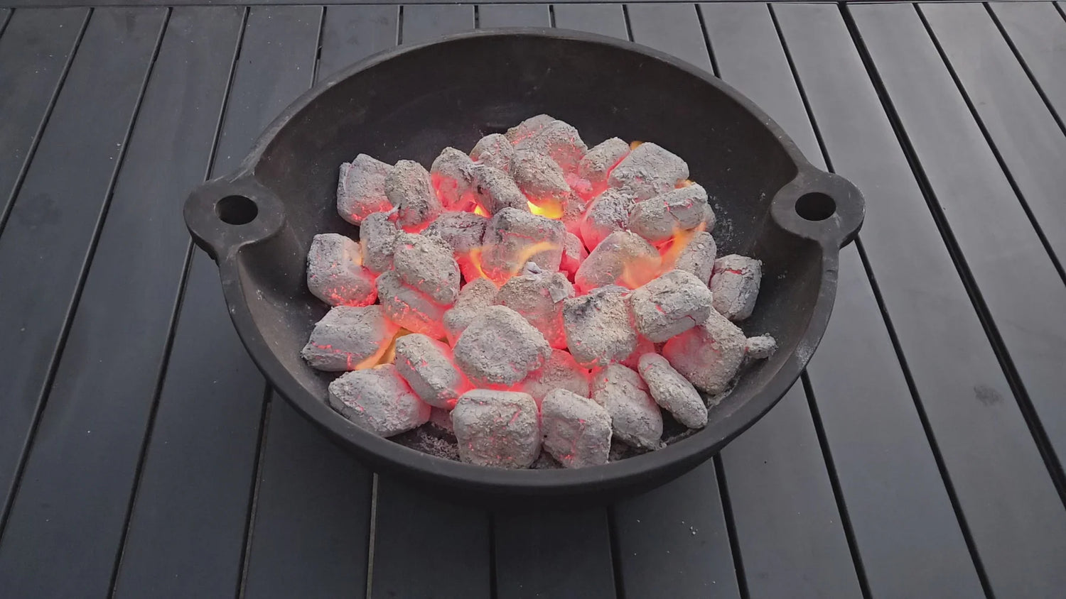Charcoal briquettes in a black metal bowl on a wooden surface