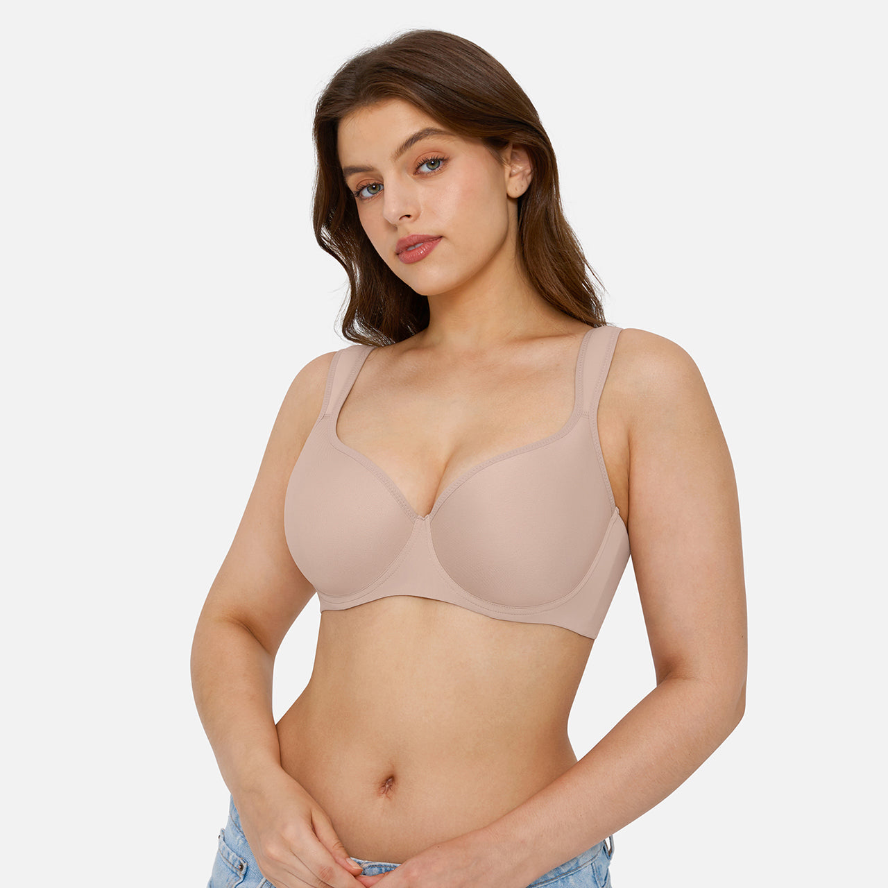 A woman modeling a seamless, underwire bra in a light beige/nude color, shown from the waist up against a solid light gray background.
