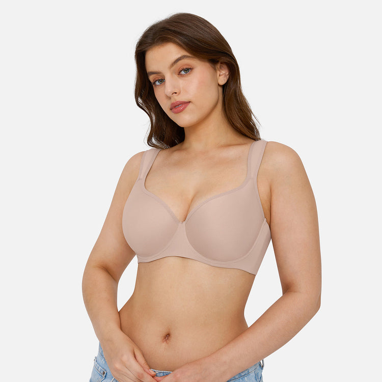 A woman modeling a seamless, underwire bra in a light beige/nude color, shown from the waist up against a solid light gray background.