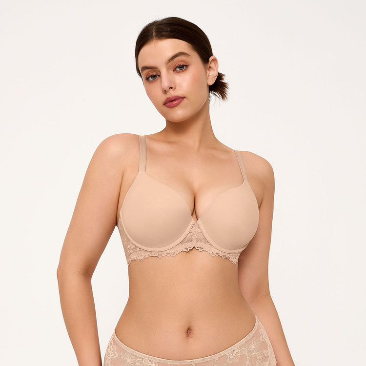 A woman modeling a beige underwire bra with lace trim and matching lace panties against a plain light background.