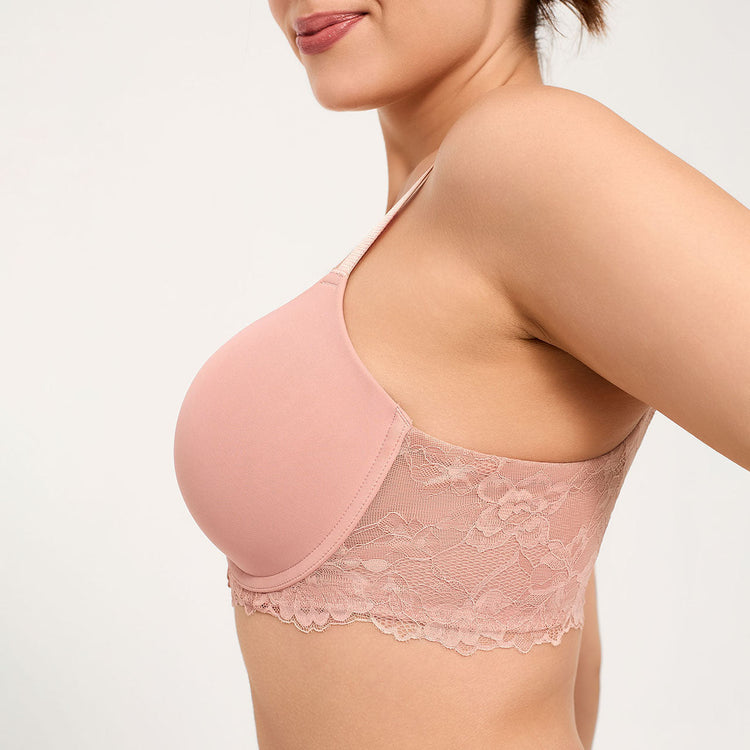 A close-up side view of a woman wearing a dusty pink underwire bra with a smooth cup and a floral lace band underband, set against a plain light background.