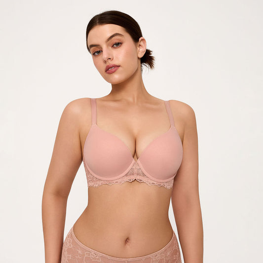 A woman modeling a light pink underwire bra with lace trim, paired with matching lace panties, against a plain light background.