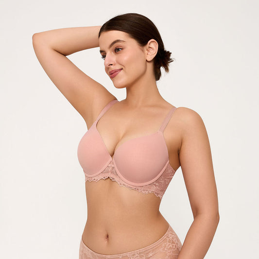 A woman modeling a light pink underwire bra with lace trim, paired with matching lace panties, against a plain light background.