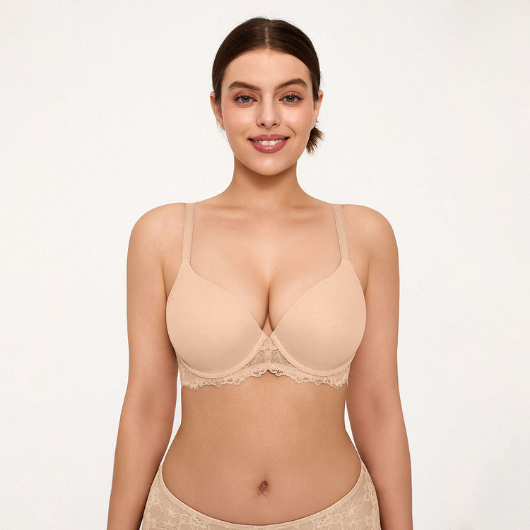 A woman modeling a light beige wireless bra with lace trim against a plain white studio background.
