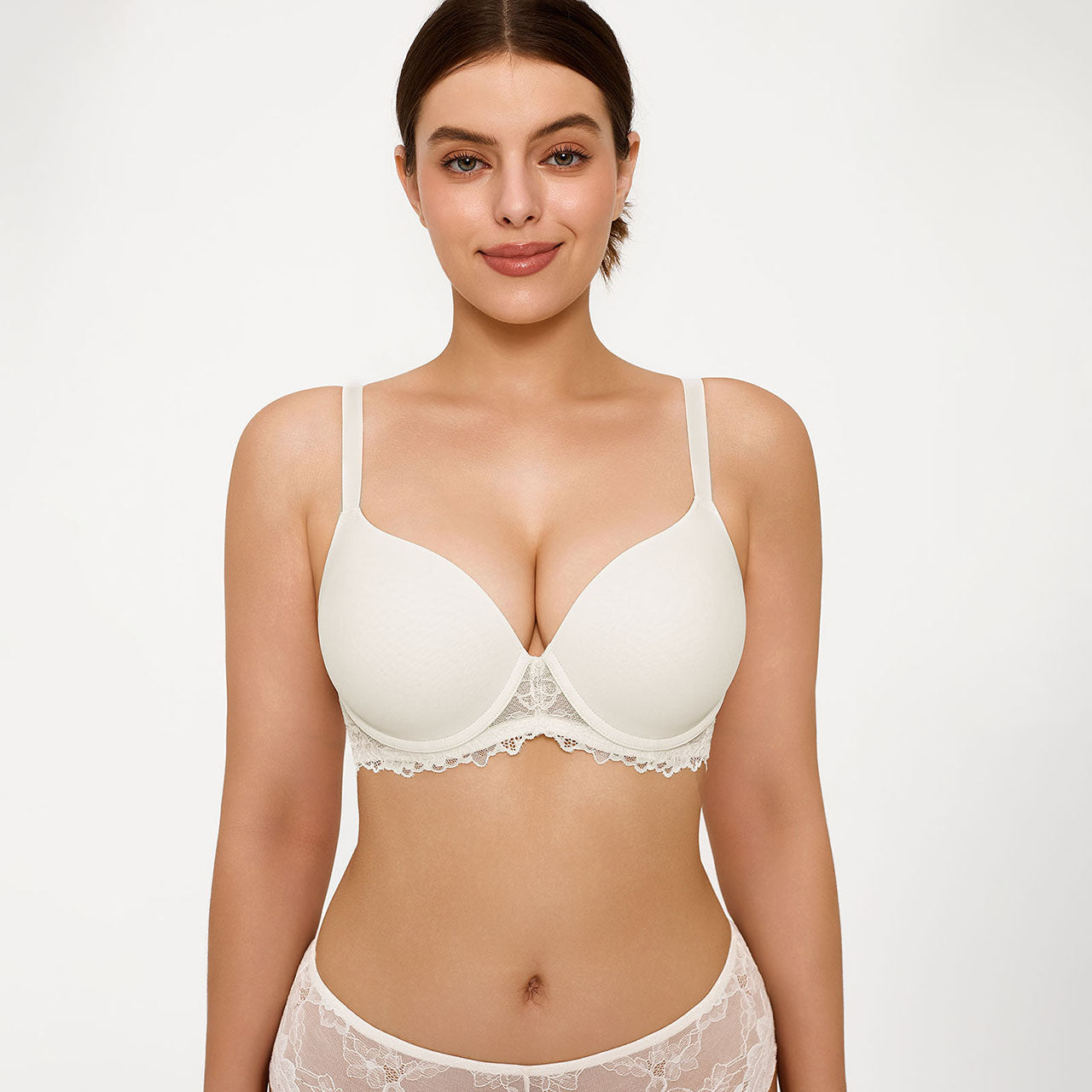 A woman modeling a white wireless underwire bra with delicate lace trim, paired with matching lace panties, against a plain light gray studio background.
