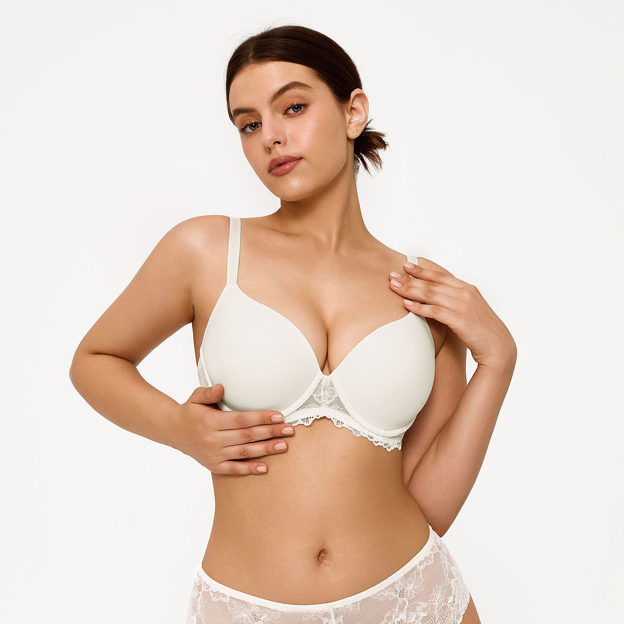 A woman modeling a white underwire bra with lace trim, paired with matching white lace panties, against a plain white studio background.