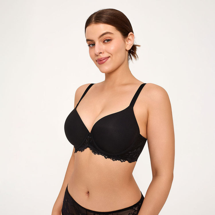A woman modeling a black underwire bra with delicate lace trim, shown from the waist up against a plain light gray studio background.
