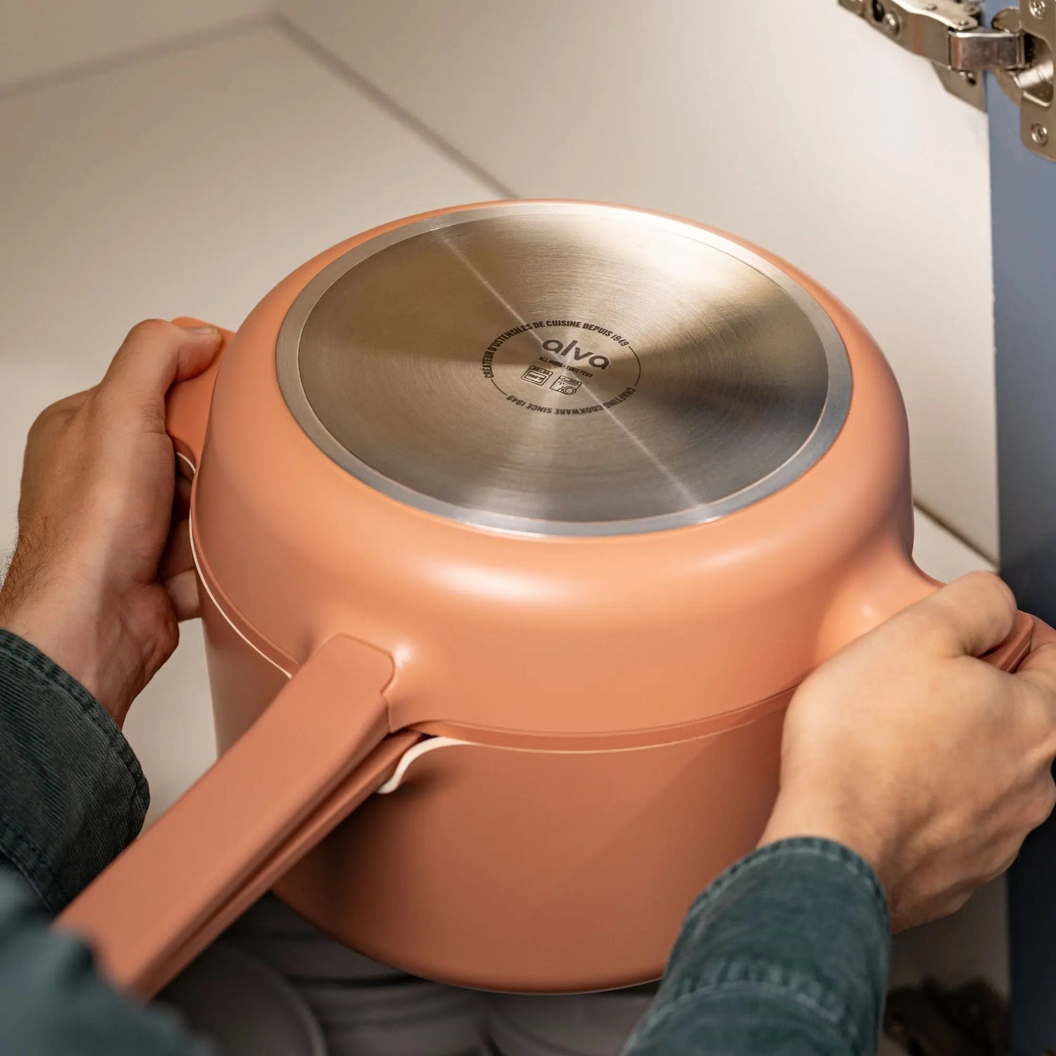 Person holding a peach-colored pot with a metallic lid, featuring the brand 'ala'.