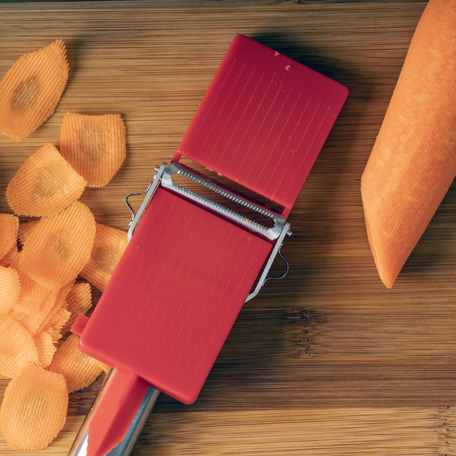 Red vegetable peeler with sliced sweet potatoes on a wooden surface