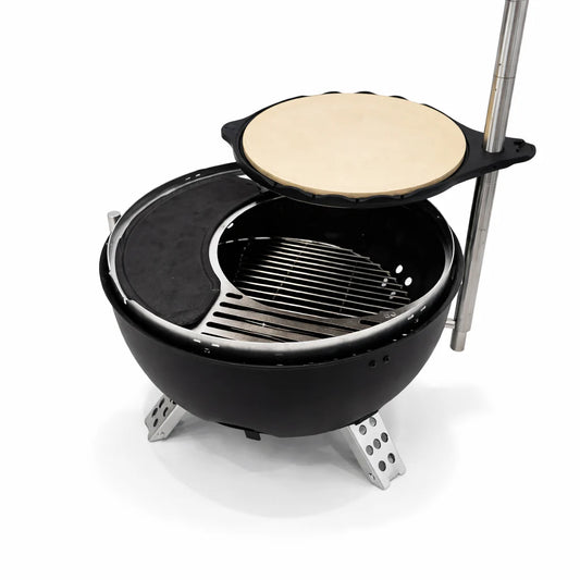 Portable pizza oven with a pizza being cooked on a stone table outdoors.