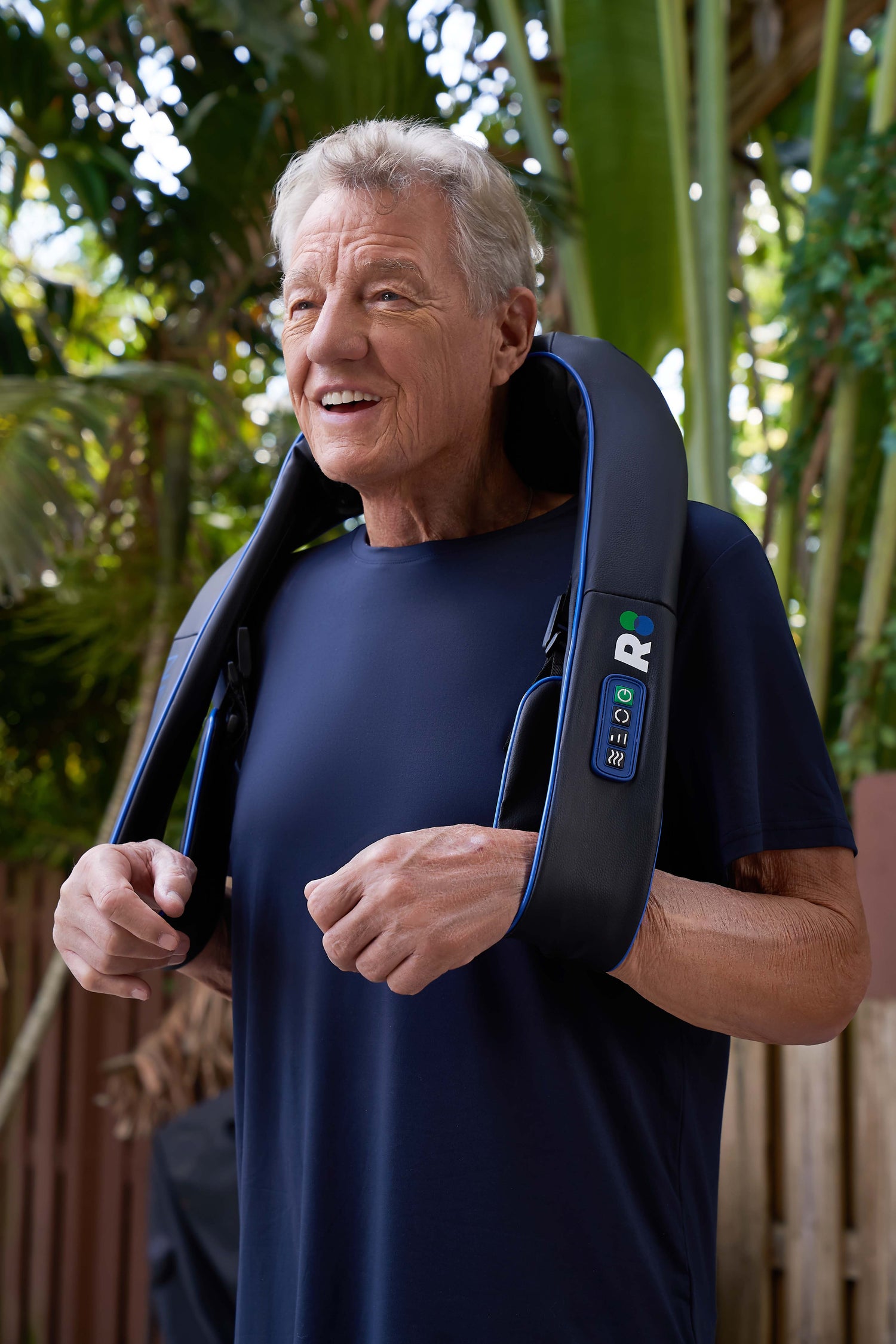 Man using a neck and shoulder massager outdoors with greenery in the background