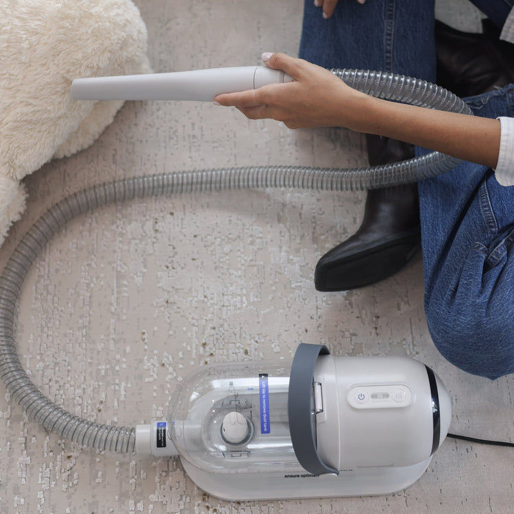 Person using a handheld vacuum cleaner on a carpeted floor.