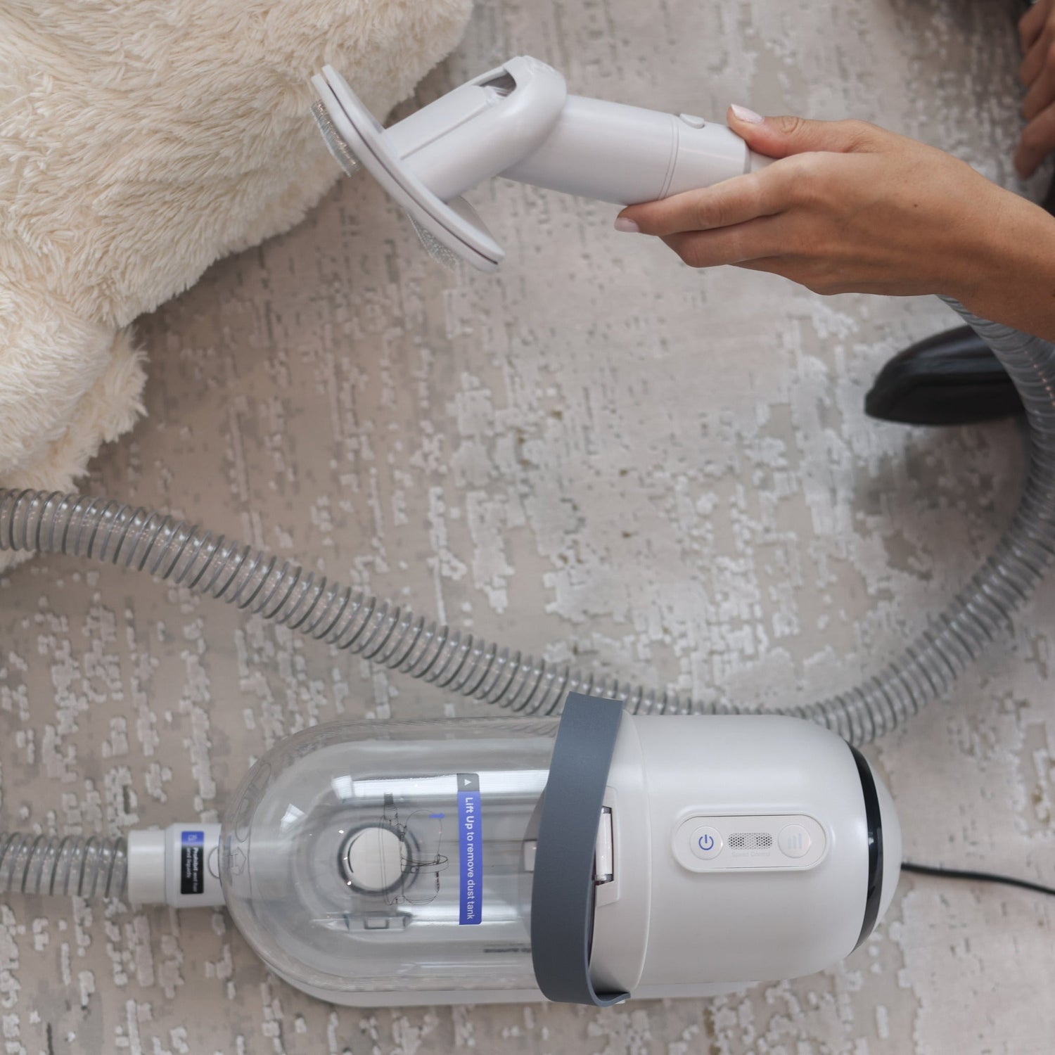 Person using a handheld vacuum cleaner on a carpeted floor.