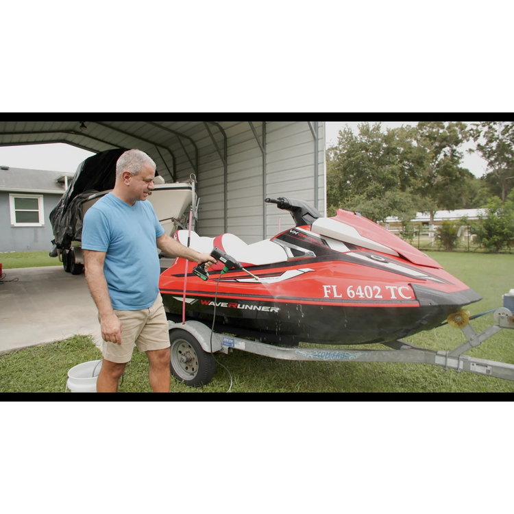 Man standing next to a red and black Avenger watercraft on a trailer in a driveway.