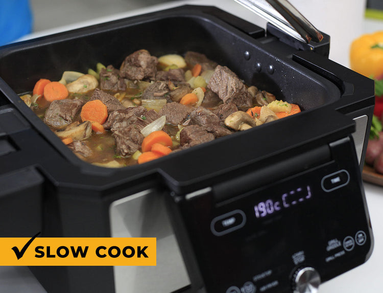 Black slow cooker with beef and vegetable stew on a white background